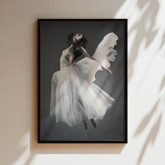 A black and white photograph of a woman in a flowing white dress, captured in mid-air with her hair blowing in the wind.