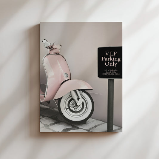 A pink Vespa scooter parked on a sidewalk, with a black sign indicating VIP parking only.