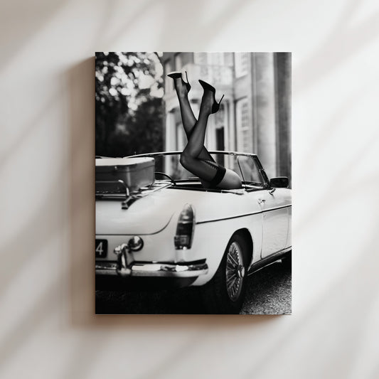 a black and white photo of a woman laying on top of a car