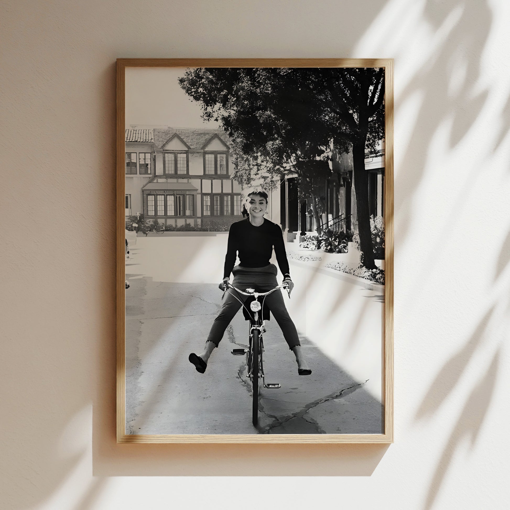A black and white photograph of a person riding a bicycle on a street, with a building and trees in the background.