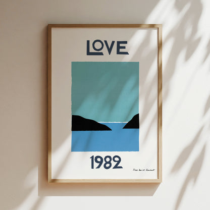 The image is a framed poster with a blue and black design depicting a serene landscape with mountains and a body of water. The text "LOVE" is prominently displayed at the top of the poster, and the year "1982" is shown at the bottom.