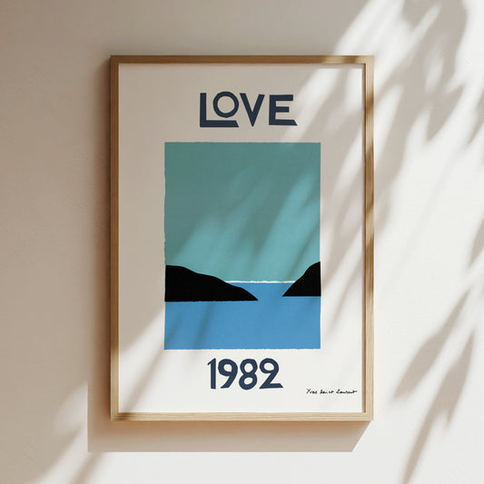 The image is a framed poster with a blue and black design depicting a serene landscape with mountains and a body of water. The text "LOVE" is prominently displayed at the top of the poster, and the year "1982" is shown at the bottom.