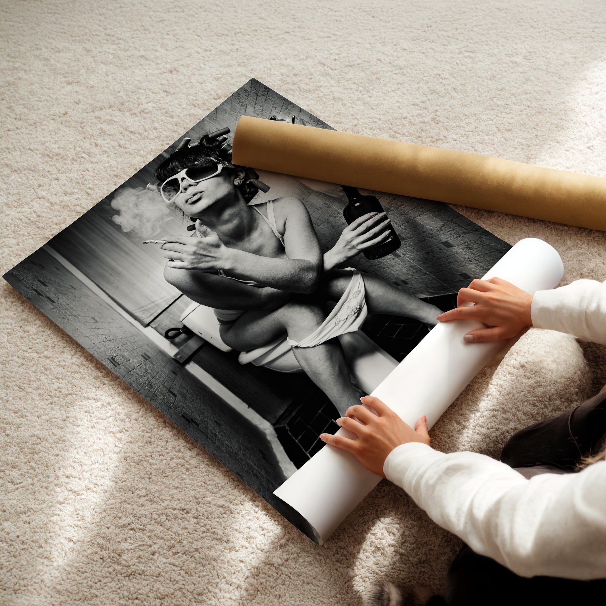 A person is holding a roll of paper and placing it under a large black and white photograph of a woman sitting on a toilet.