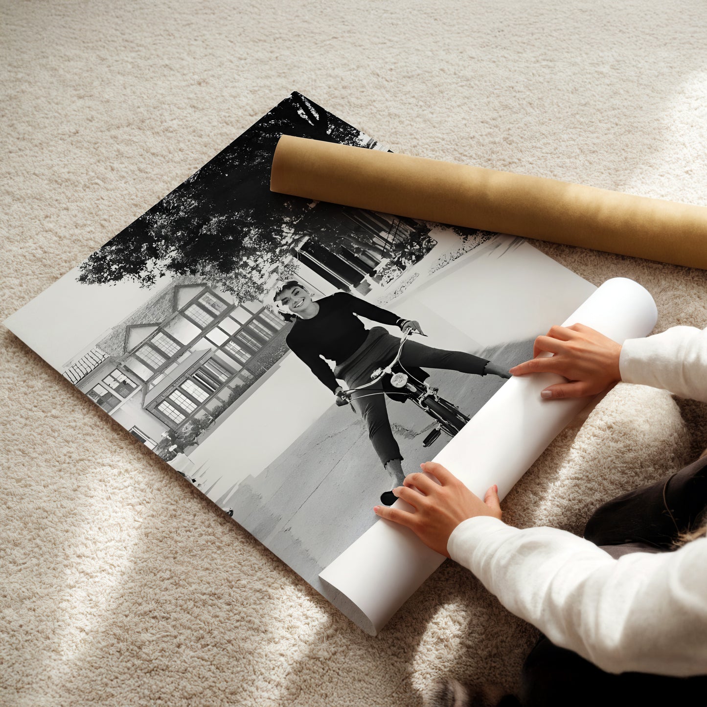 A person is holding a roll of paper and unfolding a black and white photograph of a person riding a bicycle.