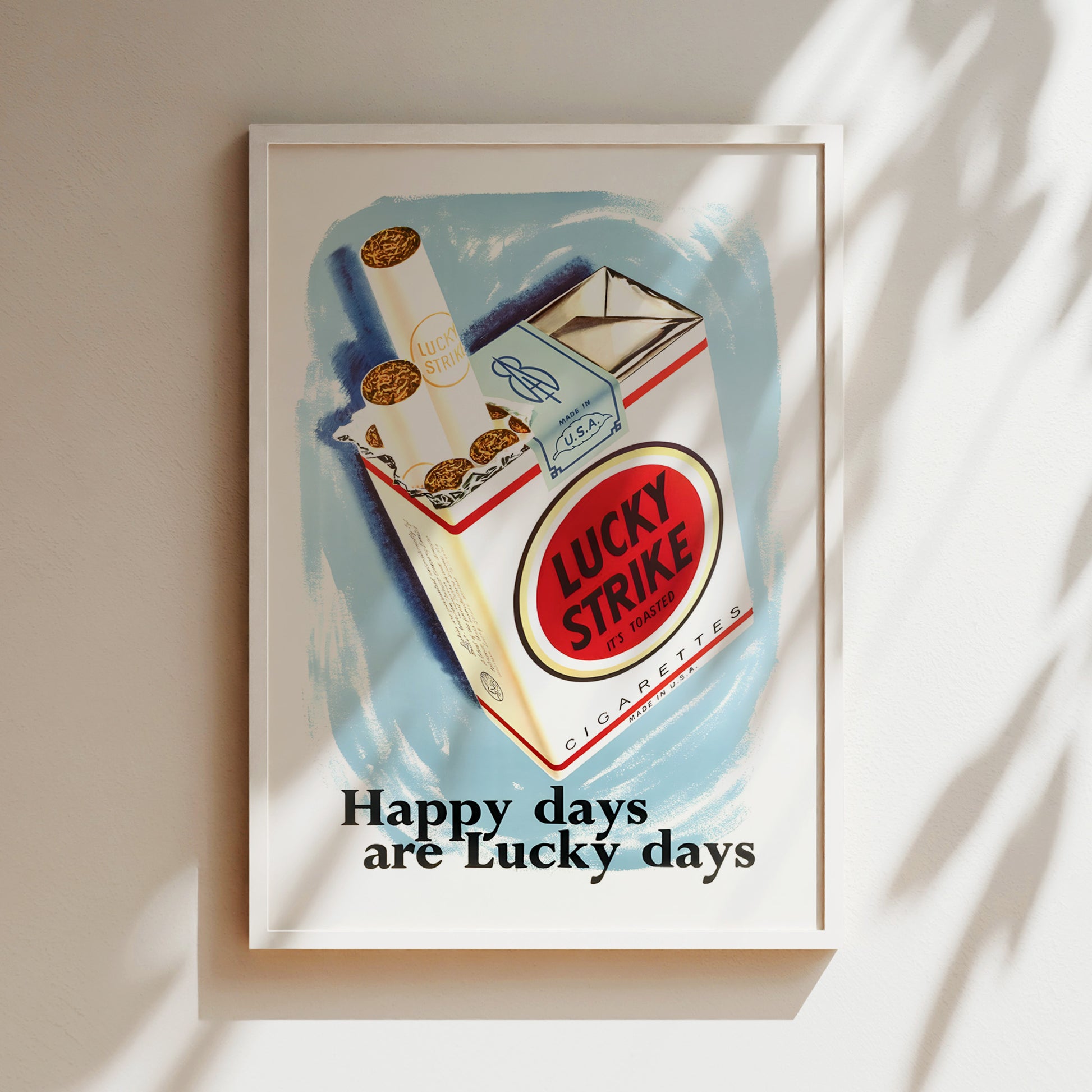 The image is a framed poster with an illustration of a Lucky Strike cigarette pack, accompanied by the text "Happy days are Lucky days".
