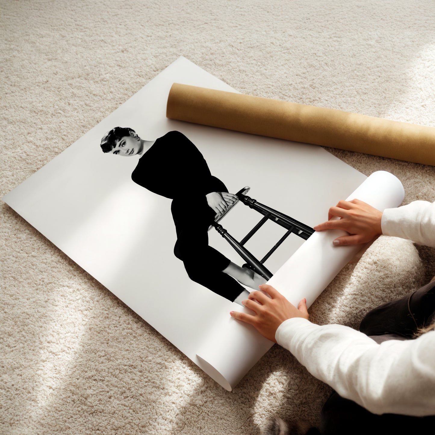A person is holding a roll of paper and placing it on top of a printed image of a woman sitting on a stool.