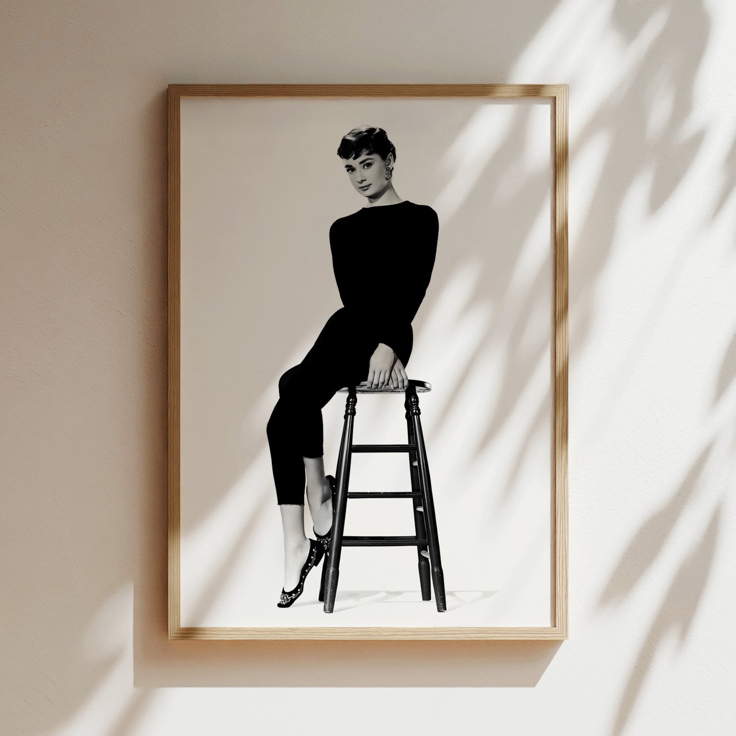 A black and white photograph of a woman sitting on a stool, wearing a long black outfit.
