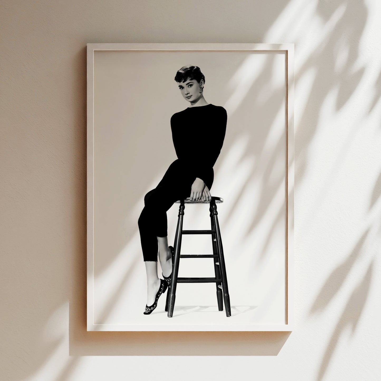 A black and white photograph of a woman sitting on a stool, wearing a long black outfit.