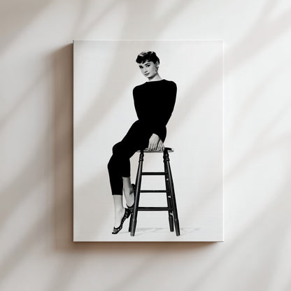 A black and white portrait of a woman sitting on a stool, wearing a long-sleeved top and pants.