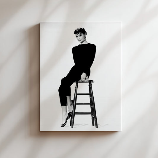 A black and white portrait of a woman sitting on a stool, wearing a long-sleeved top and pants.