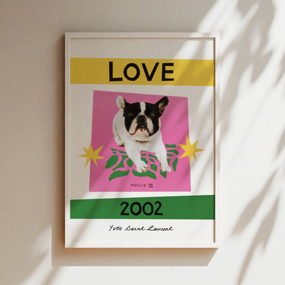 The image is a framed poster featuring a black and white dog on a pink background, with yellow and green accents. The text "LOVE" is prominently displayed above the dog, and "2002" is written below it. The poster also includes the text "MOUJK III" and "Yes Saint-Laurant" at the bottom.