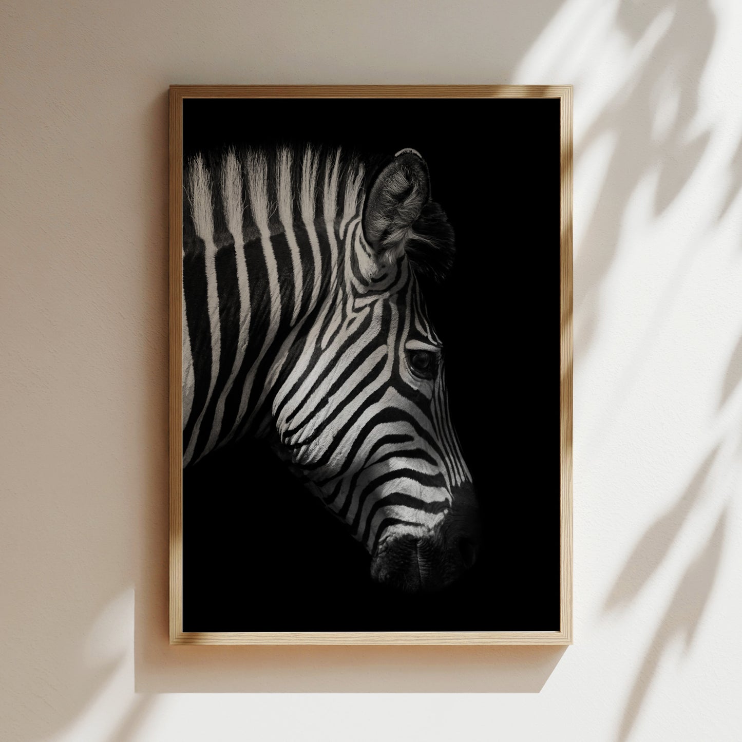 A black and white photograph of a zebra's head is displayed in a wooden frame on a white wall.