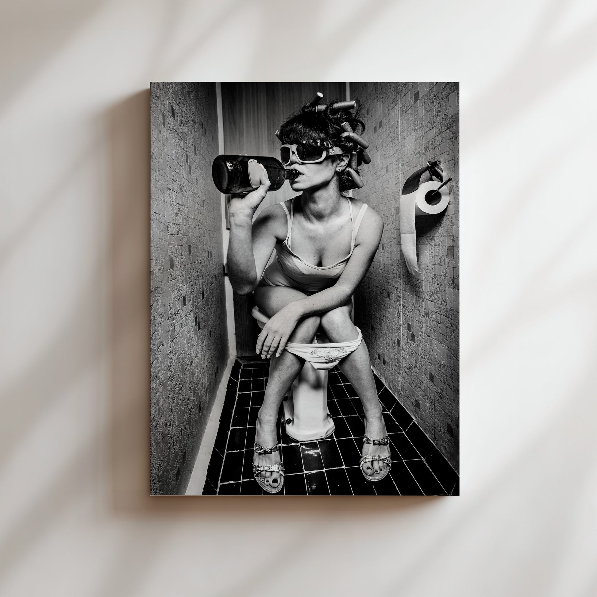 A black and white image of a woman sitting on a toilet in a bathroom, with a bottle of alcohol in her hand.