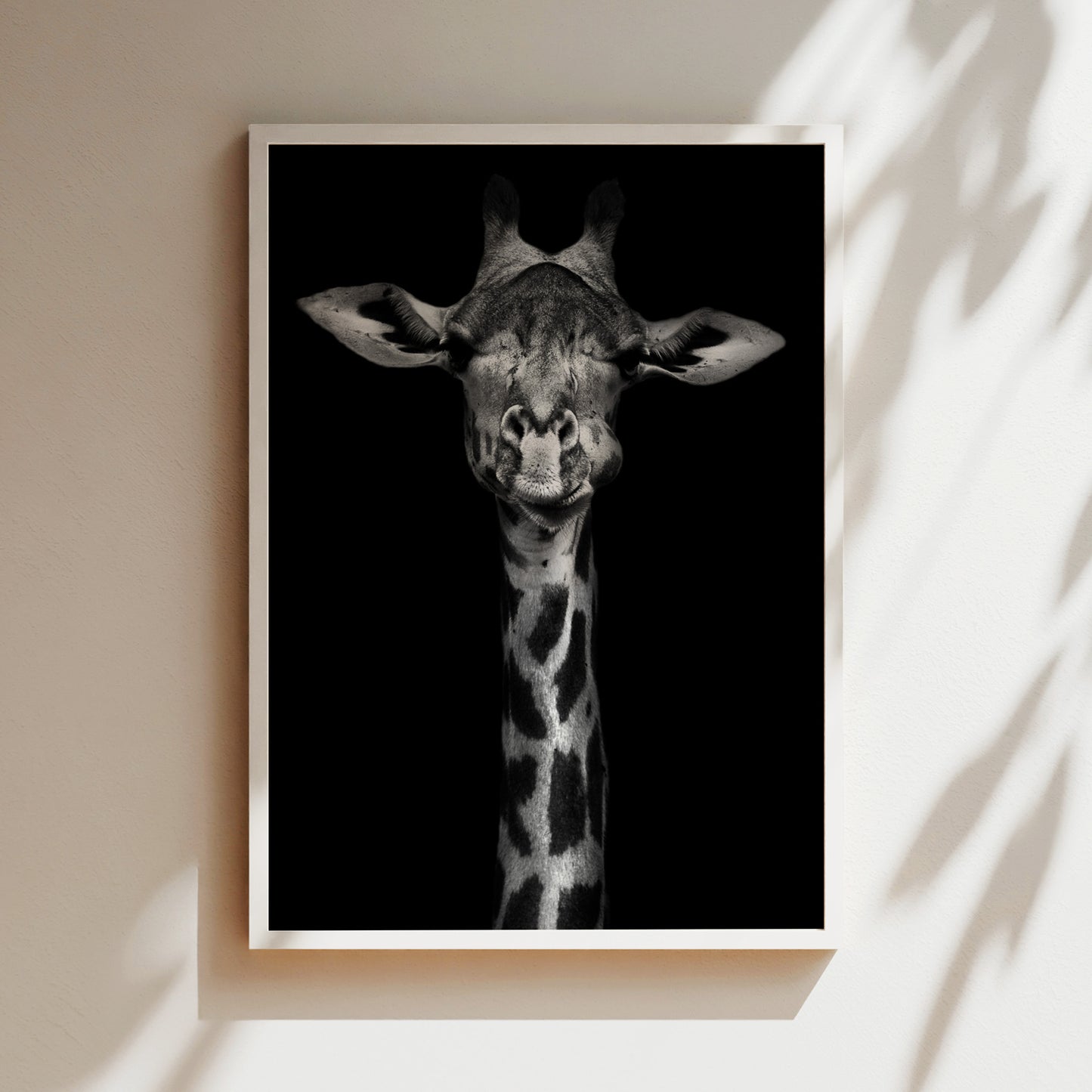 A close-up black and white photograph of a giraffe's head, with its large eyes and distinctive spotted pattern, is displayed in a frame against a dark background.