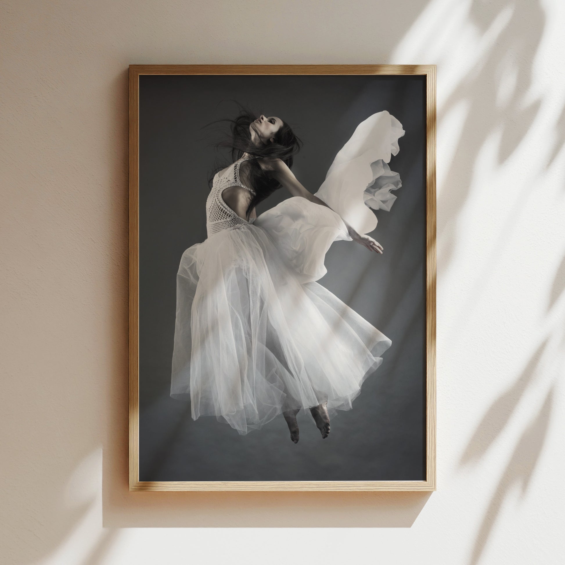 A framed black and white photograph of a woman in a flowing white dress, captured in mid-air with her hair blowing in the wind.
