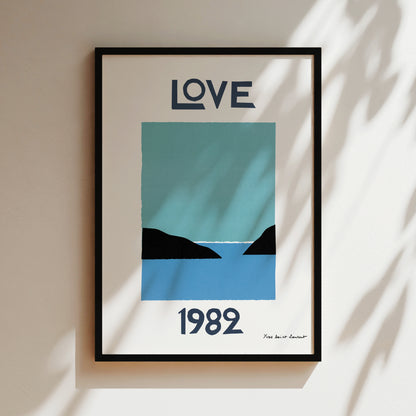 A framed poster with the word "LOVE" in large letters at the top and the year "1982" at the bottom. The poster also features a simple graphic of a blue sky and a black silhouette of a mountain.